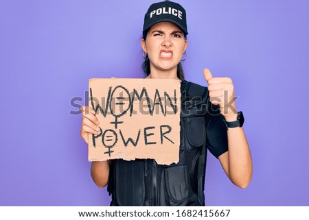 Police woman wearing security bulletproof vest uniform holding woman power protest cardboard annoyed and frustrated shouting with anger, crazy and yelling with raised hand, anger concept