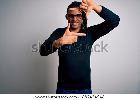 Young handsome african american man with dreadlocks wearing casual t-shirt and glasses smiling making frame with hands and fingers with happy face. Creativity and photography concept.