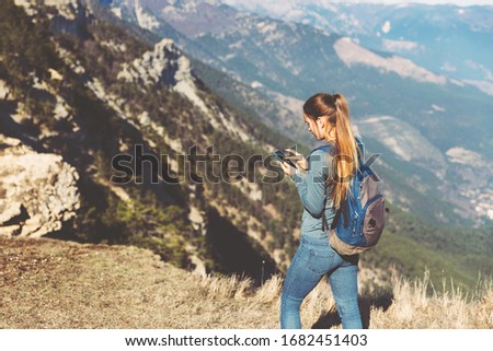 Tourist girl making a photo shoot of mountain. Young beautiful girl travels alone in the mountains in spring or autumn, looks into the distance and enjoys nature, rocks and green forests, view of the