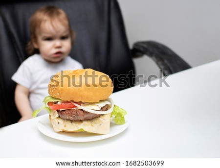 Dissatisfied Blurry, out of focus toddler kid looking at a big burger. selective focus.