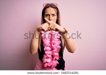 Young beautiful blonde woman wearing swimsuit and floral Hawaiian lei over pink background Rejection expression crossing fingers doing negative sign