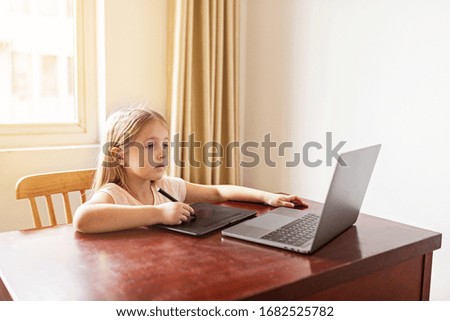 Pretty schoolgirl studying homework during her online lesson at home, social distance during quarantine covid-19, self-isolation, online education concept, home schooler. Workplace in living room.