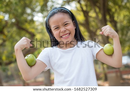 photo happy Little asian girl child standing with big smile. girl with green apple showing biceps.
fresh healthy green bio background with abstract blurred foliage and bright summer sunlight