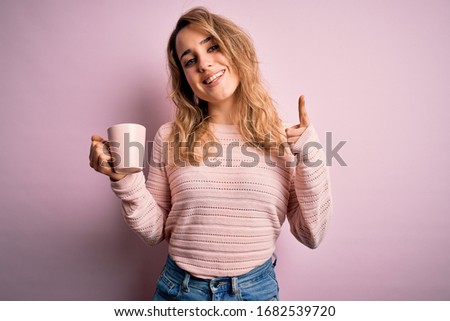 Young beautiful blonde woman drinking mug of coffee over isolated pink background surprised with an idea or question pointing finger with happy face, number one