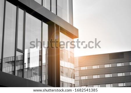 Modern office building wall made of steel and glass with blue sky. Glass surface with sunlight. Black and white.