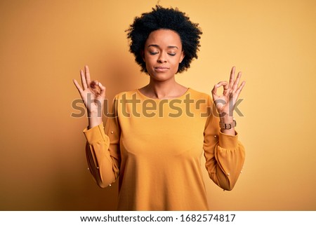 Young beautiful African American afro woman with curly hair wearing casual t-shirt relax and smiling with eyes closed doing meditation gesture with fingers. Yoga concept.