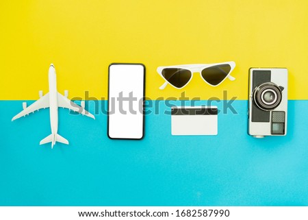 Summer holiday and travel concept. Top view of black smartphone and glasses with camera on blue color background.	