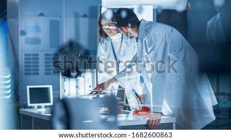Diverse International Team of Industrial Scientists and Engineers Wearing White Coats Working on Heavy Machinery Design in Research Laboratory. Professionals Using 3D Printer, Computers and Microscope