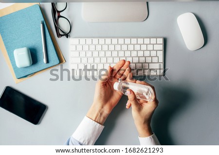 Close-up of hands using antiseptic gel to disinfect hands over a work desk in an office. Preventive measures during the period of epidemic and social exclusion. Royalty-Free Stock Photo #1682621293
