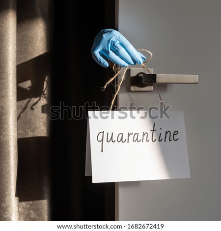 A hand in a latex blue glove hangs a sign on paper with the signature Quarantine. The concept of self-isolation during a pandemic and epidemic.