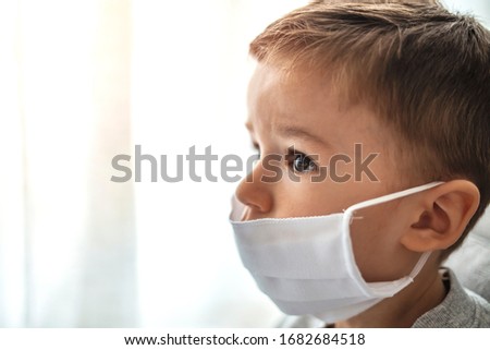 Toddler boy with medical mask on the face. Covid 2019 corona virus outbreak. Sad child isolated on white. Boy at home. Little boy trying to stay healthy by wearing a mask