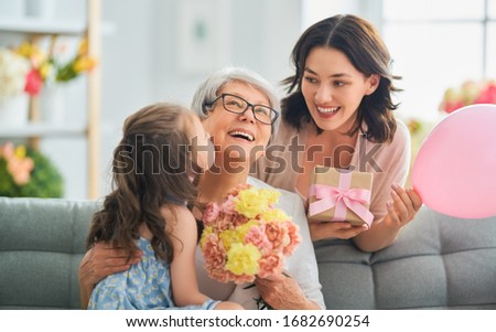 Happy mother's day! Child daughter is congratulating mom and granny giving them flowers and gift. Grandma, mum and girl smiling and hugging. Family holiday and togetherness.                        