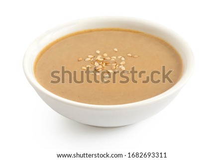 Tahini in a white ceramic bowl sprinkled with sesame seeds isolated on white. Royalty-Free Stock Photo #1682693311
