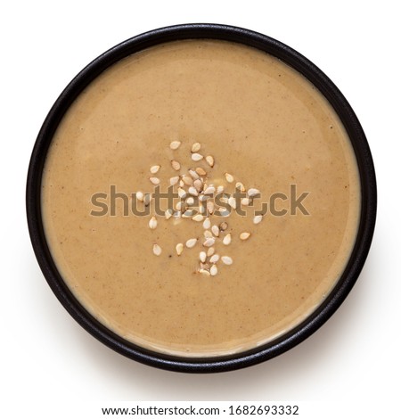 Tahini in a black ceramic bowl sprinkled with sesame seeds isolated on white. Top view. Royalty-Free Stock Photo #1682693332
