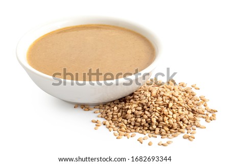 Tahini in a white ceramic bowl next to a pile of sesame seeds isolated on white. Royalty-Free Stock Photo #1682693344