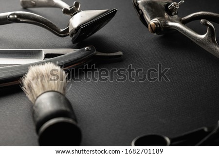 On a black surface are old barber tools. Two vintage manual hair clipper, razor, shaving brush, hairdressing scissors. black monochrome.