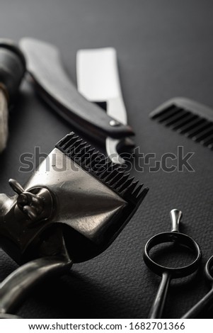 On a black surface are old barber tools. two vintage manual hair clipper, comb, razor, shaving brush, hairdressing scissors. black monochrome. vertical