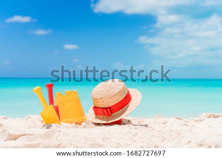 Kid's beach toys, hat and sunglasses on white sandy beach background the sea