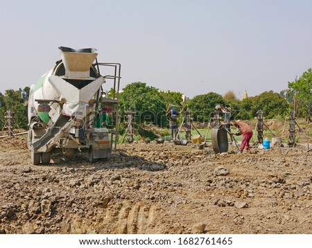 A construction site with a cement mixer truck with workers working outdoor to build a concrete fence 