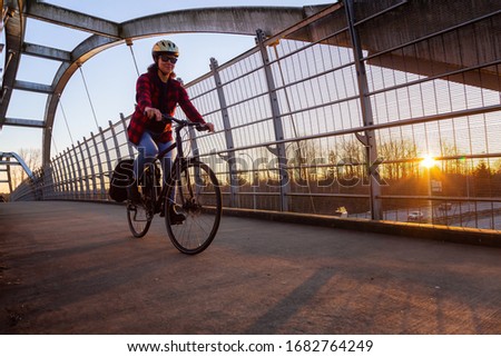 Caucasian Woman Riding a Bicycle on a Pedestrian Bridge over the Highway during a sunny sunset. Taken in Surrey, Vancouver, British Columbia, Canada.