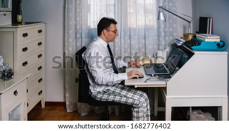 Man working from home with laptop wearing shirt, tie and pajama pants Royalty-Free Stock Photo #1682776402