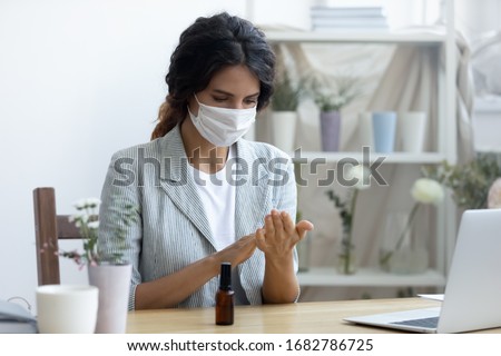 Female employee wear protective medical mask use hand sanitizer from covid-19 coronavirus pandemic, woman worker in face cover sanitize with liquid antibacterial gel in office, corona virus concept Royalty-Free Stock Photo #1682786725