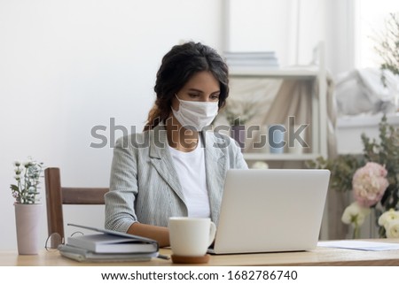 Female employee wear medical protective mask from covid-19 coronavirus pandemic work on laptop in office, woman in face cover from corona virus busy using computer at workplace, epidemic concept Royalty-Free Stock Photo #1682786740