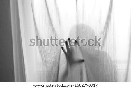 A shadow of a mysterious person behind the curtain