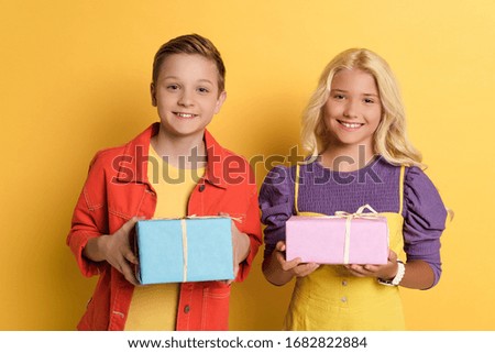 smiling friends holding gift boxes on yellow background