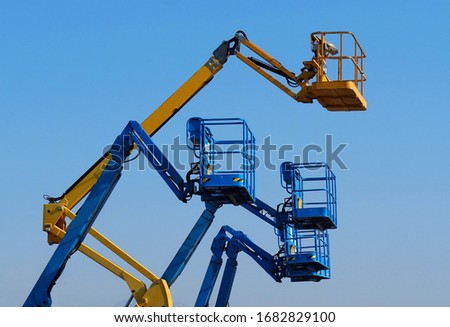 Work aerial platforms against blue cloudless sky. One cherry picker yellow among three blue Royalty-Free Stock Photo #1682829100