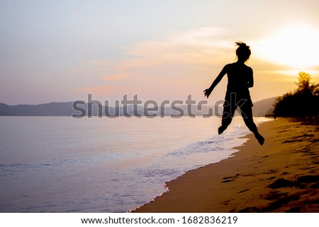 Silhouette photography of woman jumping at the sand beach next to the sea during sunset.