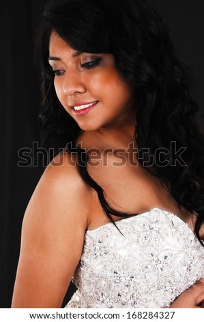 A closeup picture of a Hispanic young woman with long black hair standing for black background in a wedding dress. 