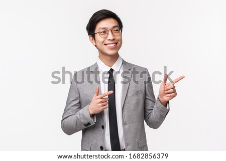 Waist-up portrait of pleased successful asian businessman, office manager presenting his idea on team building meeting, smiling satisfied, pointing and looking right, white background
