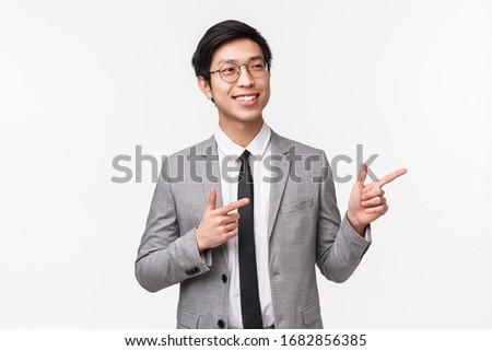 Waist-up portrait of successful, professional asian male entrepreneur, office clerk in grey suit, seeing pleasant numbers at chart, pointing and looking pleased presentation, show right advertisement
