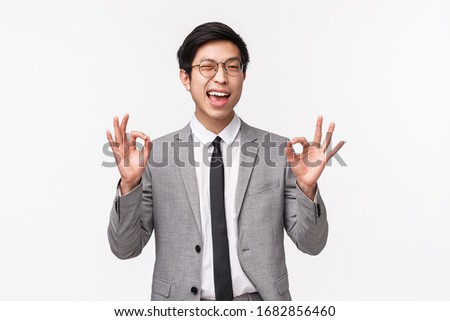 Waist-up portrait of carefree, unbothered and assured young asian male office manager, businessman assure client everything under control, guarantee safety and quality, show okay signs and wink