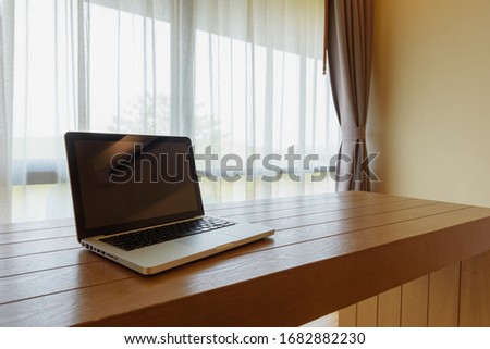 Laptop computer on an office desk with a large window on the background
