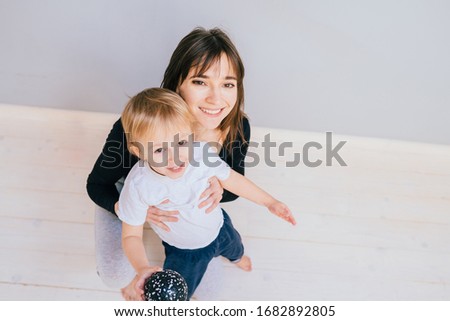 Brunette mother and child in sport clothing sitting together lokking at camera showing ball pilates toning equipment in studio over grey wall background. Top view. Copy space