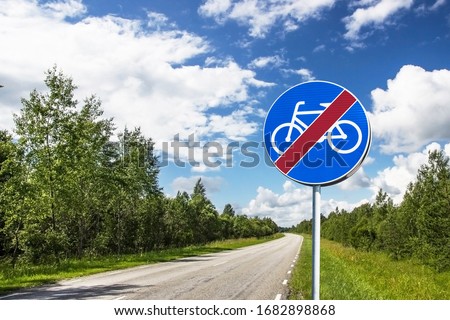 
End of cycle path sign. Blue round road sign with red strikethrough cross out line. No cycling long asphalt road summer landscape.