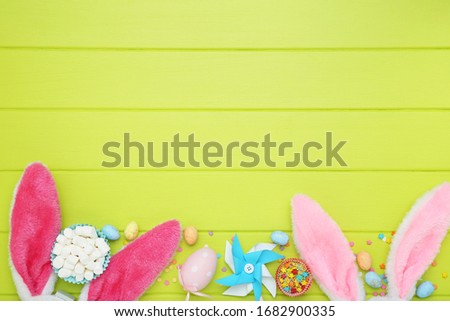 Easter concept. Rabbit ears with eggs, sprinkles and marshmallows on green wooden table