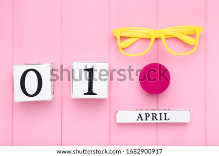 April Fool's Day concept. Wooden calendar with eyeglasses and soft nose on pink background