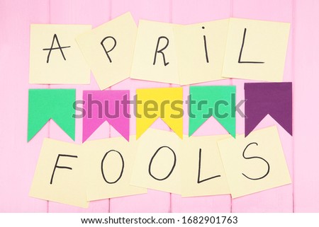 Text April Fool's Day with colorful paper flags on pink wooden background