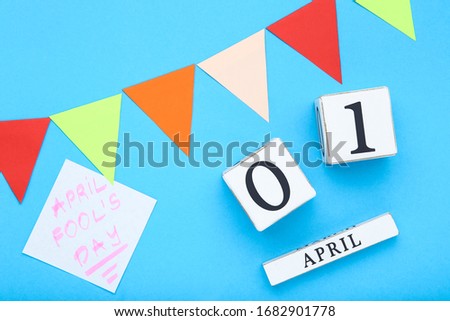 Text April Fool's Day with wooden calendar and paper flags on blue background