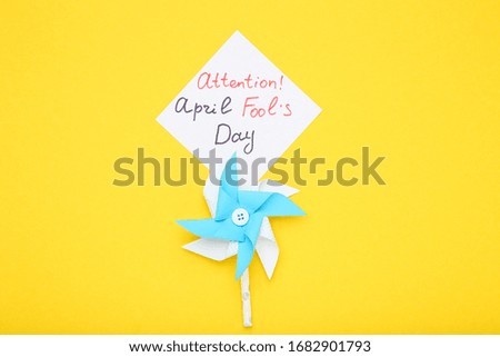 Text Attention April Fool's Day with paper windmill on yellow background