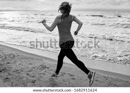 Back view of young fitness woman runner running at seaside, copy space. Girl working out on beach at summer morning, full length portrait. Healthy lifestyle concept