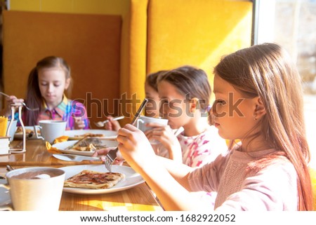 Preteen group of child sit in cafe or home in morning and eat sweet pancakes . Young people  smiling 