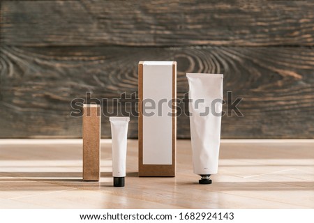 Two cosmetic white tubes and craft paper boxes on wooden table. Brand package layout. Closeup, copyspace for text