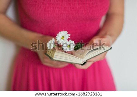 Girl holding in her hands an open little book and flowers. Reading and education in free time. 