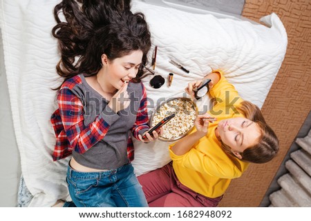 Two young women are at home, lying on the bed, talking and resting. The view from the top. The concept of quarantine, work from home, security and isolation