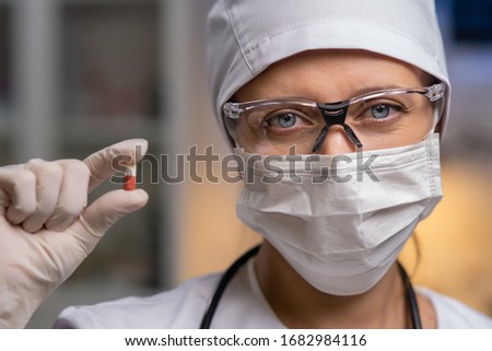 Female Doctor In Laboratory Office On Background Of Test Tubes And Medical Equipment On Background Of Test Tubes And Medical Equipment Masked Gloves And Glasses Holds Pills In Hands