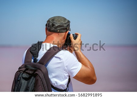 A man stands back with a backpack taking photos of nature, salty pink lake.